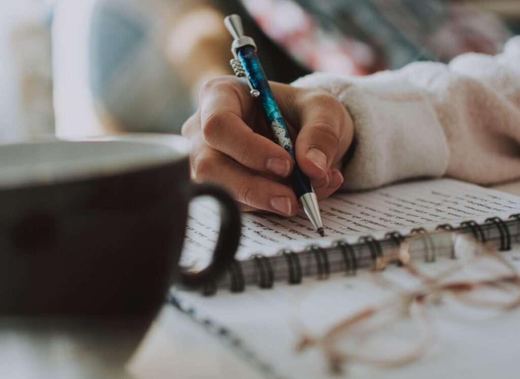 Notebook on a desk with a woman's hand writing in it, illustrating the simplicity of brain dumping.