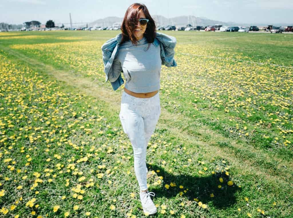 Woman walking through a field, smiling and wearing casual clothes, representing the benefits of movement and fresh air.