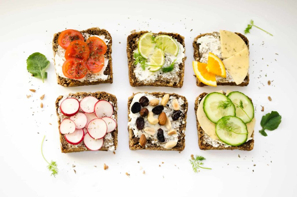 Overhead shot of six pieces of toast with various healthy toppings like tomatoes and cucumbers, illustrating an easy way to nourish yourself.