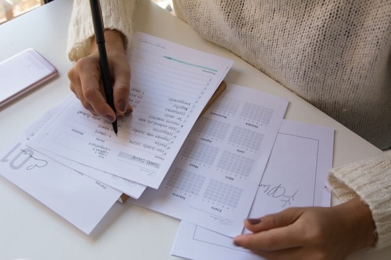 Overhead view of a woman's hands writing on a piece of paper, with scattered sheets underneath, symbolizing proactive planning to ease Sunday scaries.