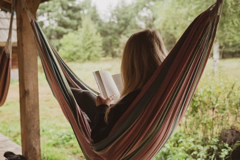 Woman reading in a hammock, seen from behind, appearing relaxed, illustrating the importance of unwinding to reduce stress.