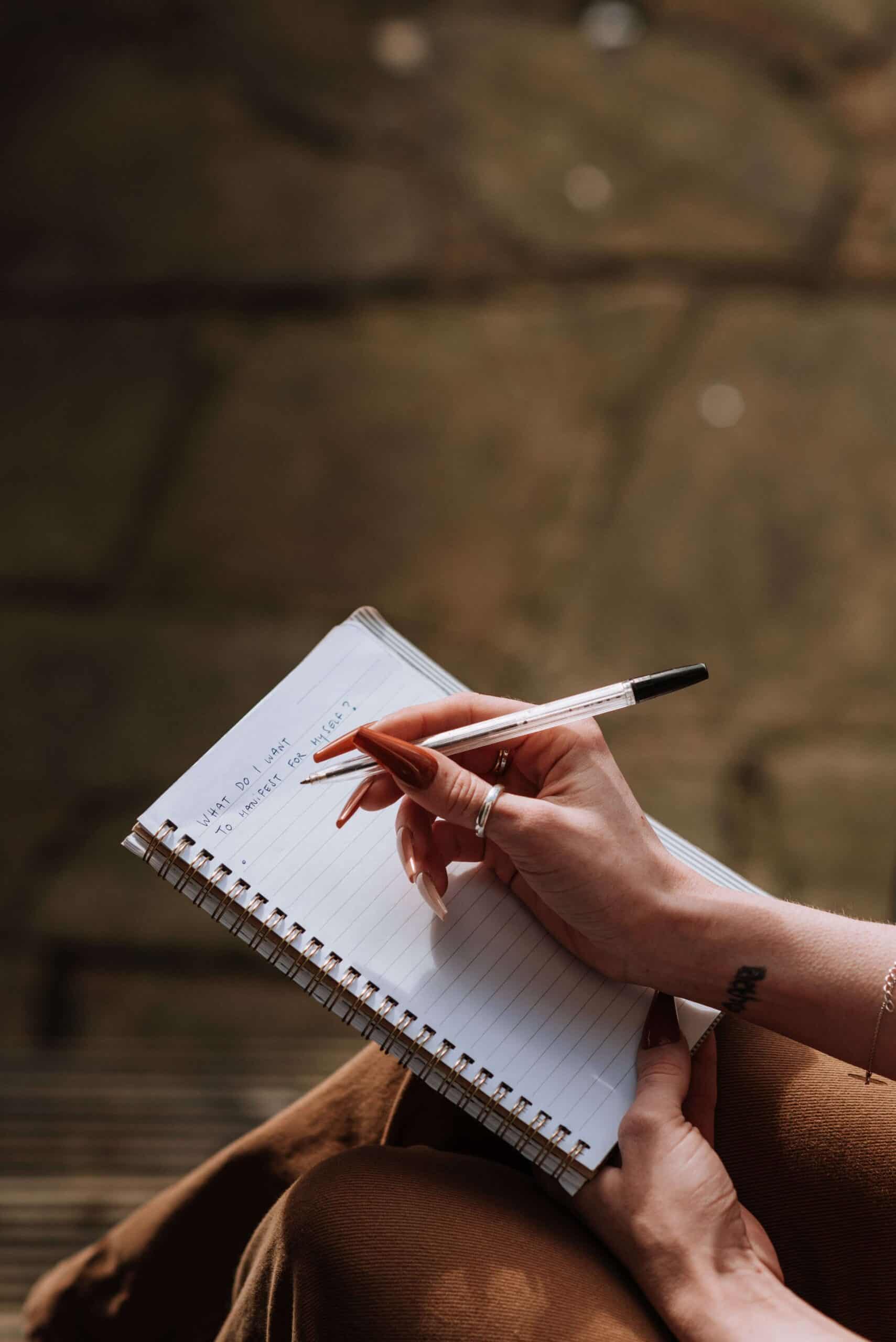 Woman’s right hand writing in a notebook while holding it on her lap, representing the practice of brain dumping.