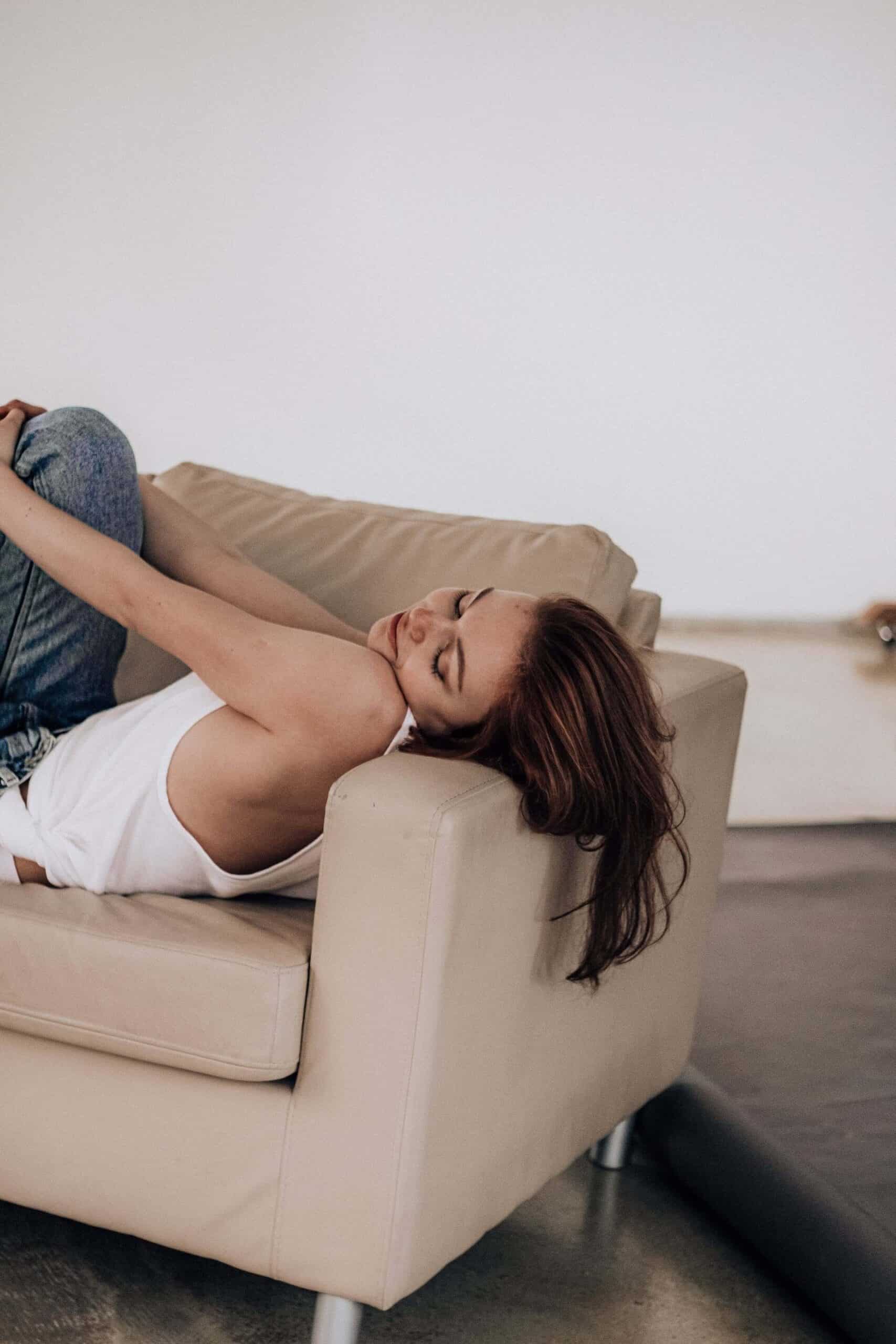 Woman lying on a sofa with her head on the armrest, hugging her knees and smiling blissfully, representing the relief of overcoming morning anxiety.