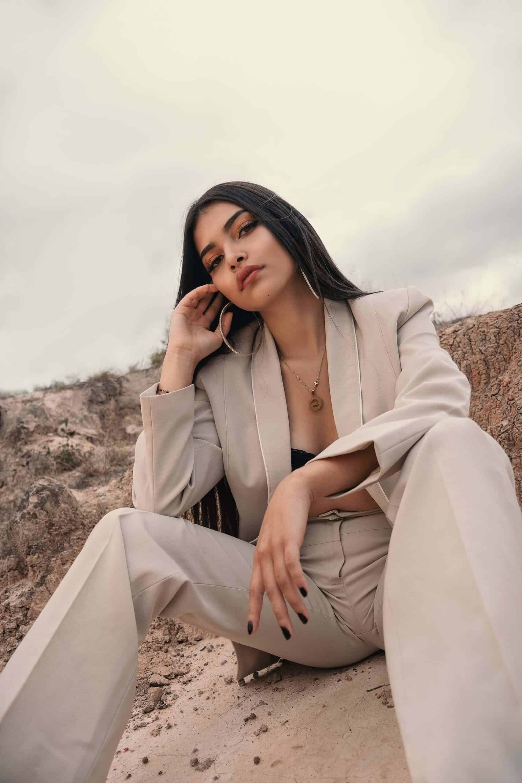 Woman in a tan power suit sitting on a rock in a canyon, looking stylish and confident, representing the effortless appeal of that girl.