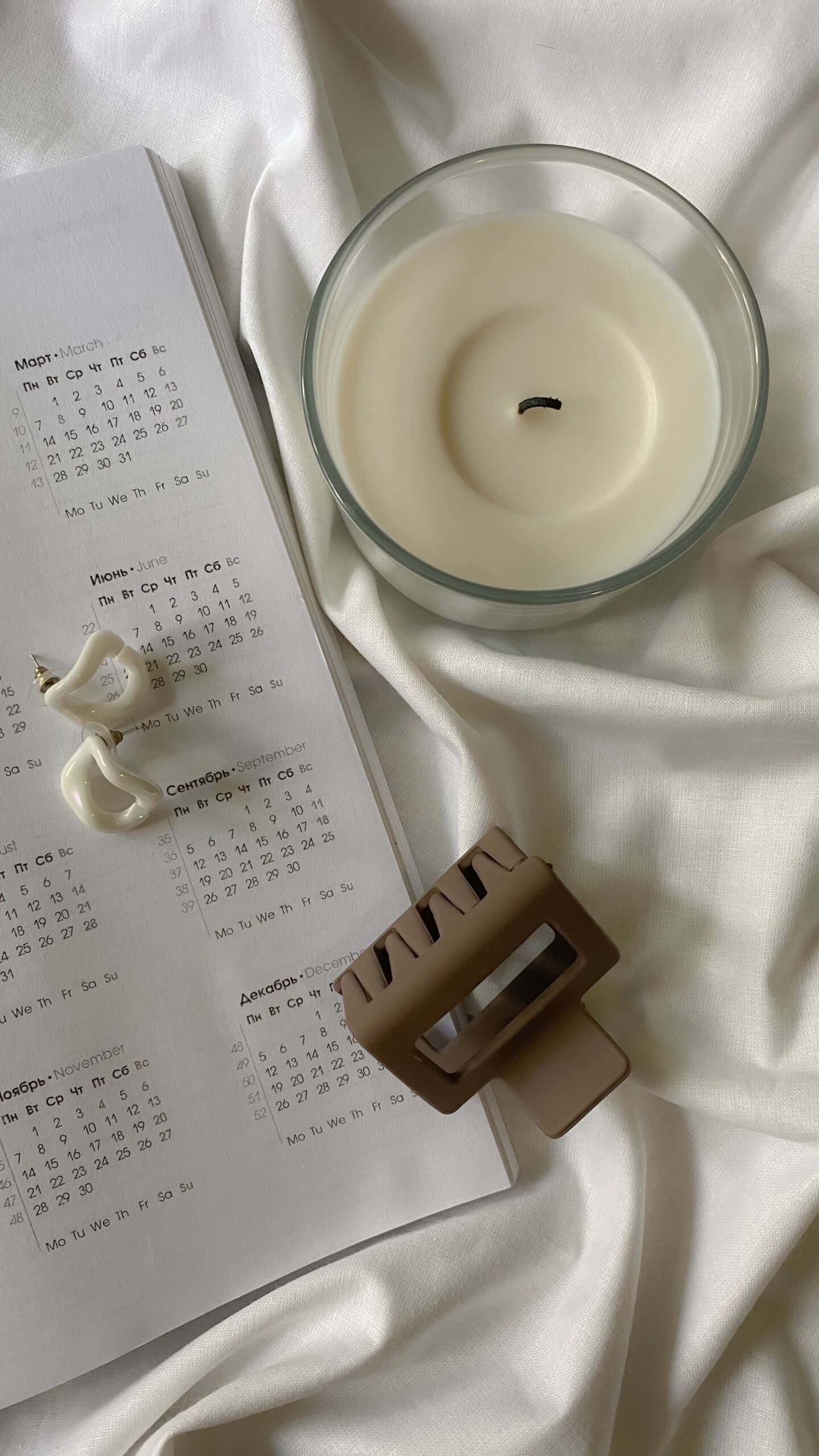 Flat lay of an open planner partially in view, alongside a candle, a hair clip, and a small sculpture, evoking an aspirational and organized life reset.