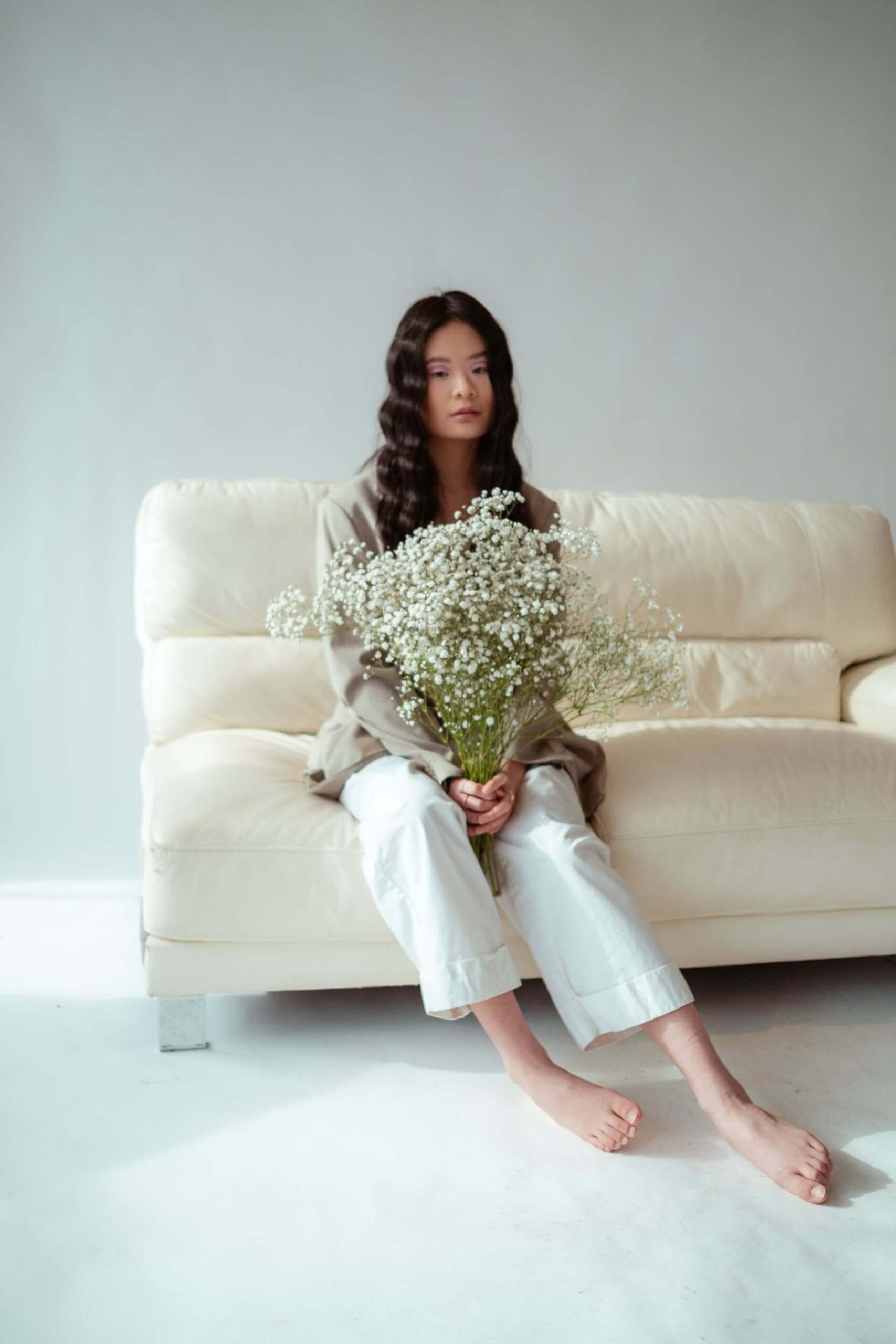 A barefoot woman on a sofa holding white flowers, embodying unique self-care ideas in a calming environment.