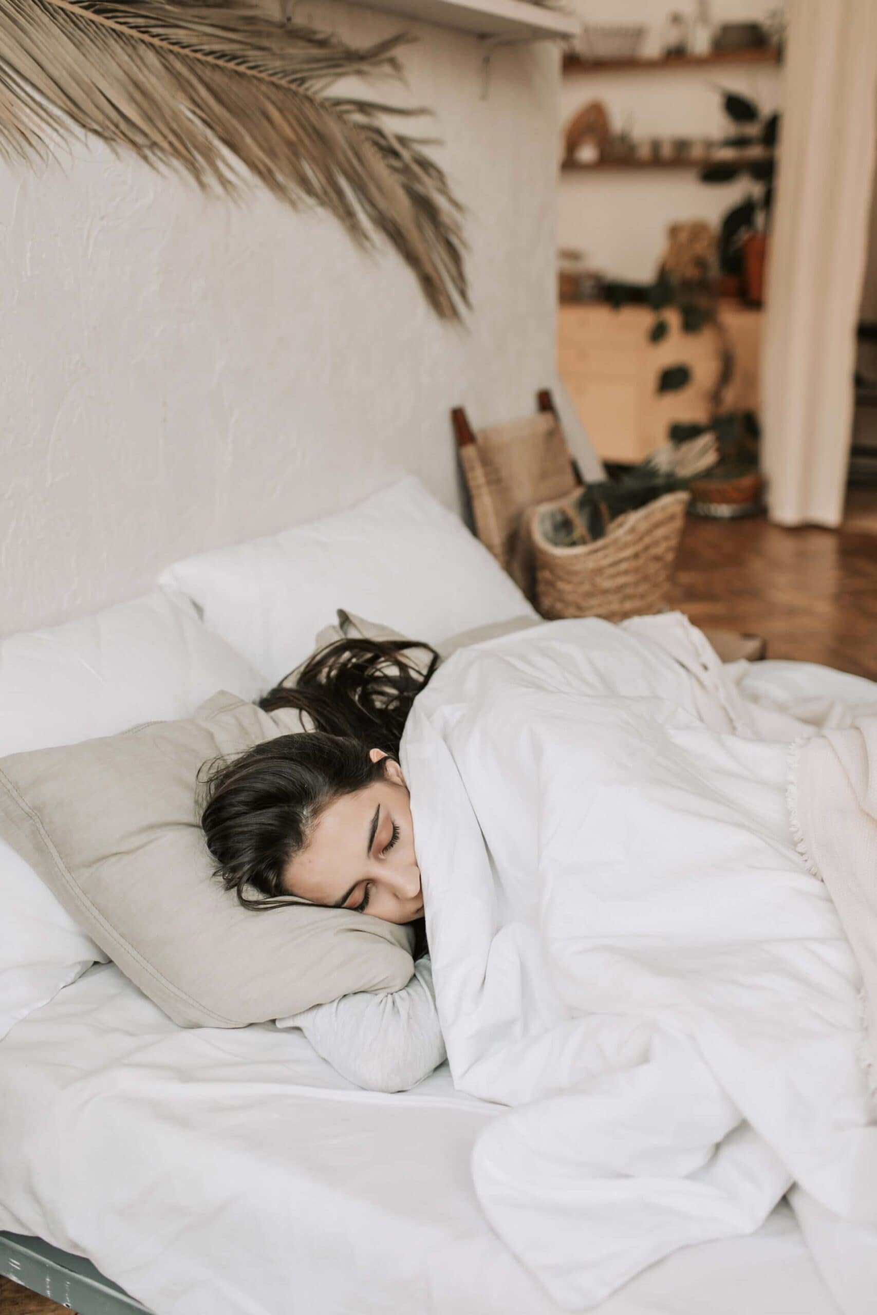 A cozy woman in bed with the covers up to her nose, looking calm and restful, representing a peaceful morning routine.