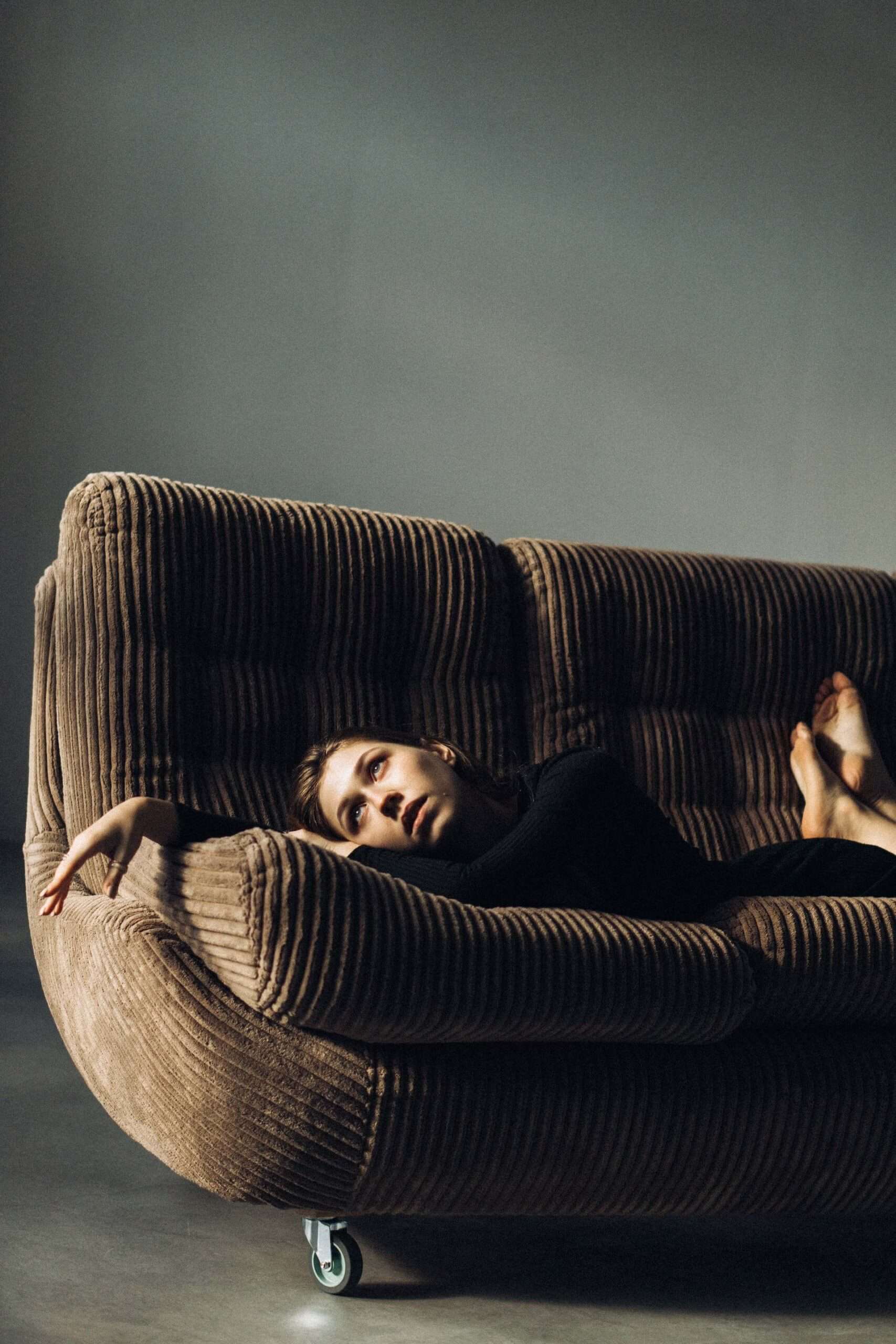 Woman lying on her stomach on a sofa, looking up with a sad expression, reflecting on strategies to survive a bad day.