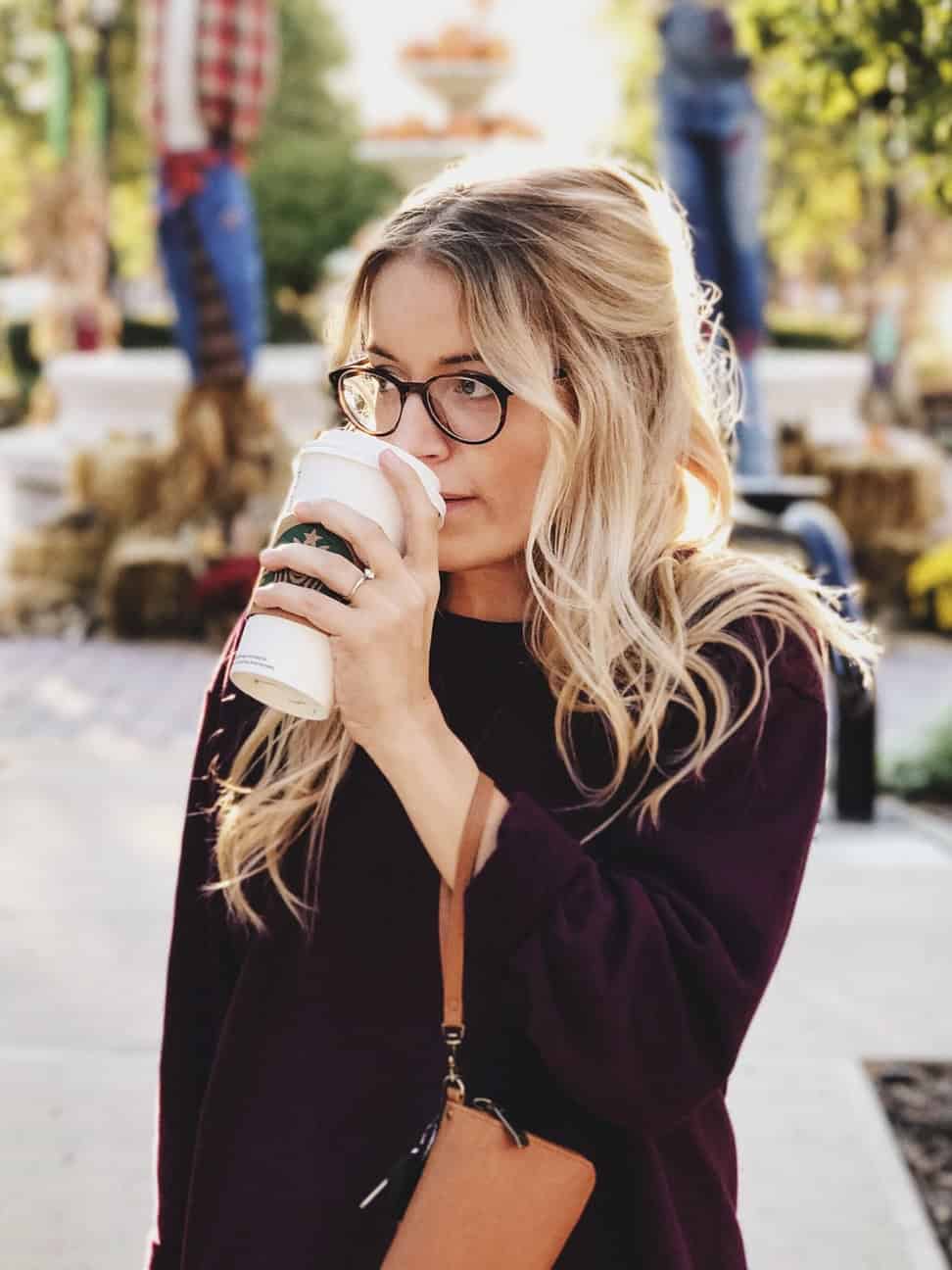 A woman walking outdoors with a paper coffee cup to her lips, looking to the right and appearing relaxed and content, embodying the joy of self-care.