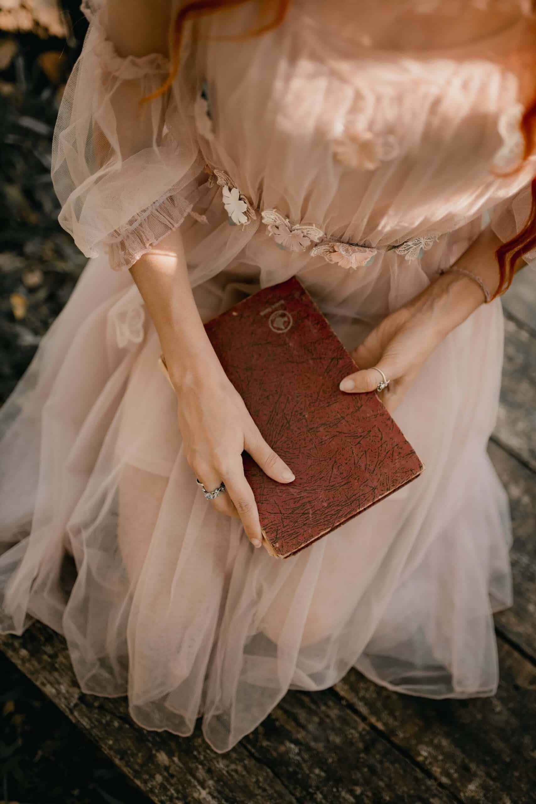 A faceless woman wearing an ethereal pink dress, sitting on her knees with a journal in her hands, symbolizing aspiration and reflection to spring clean your life.