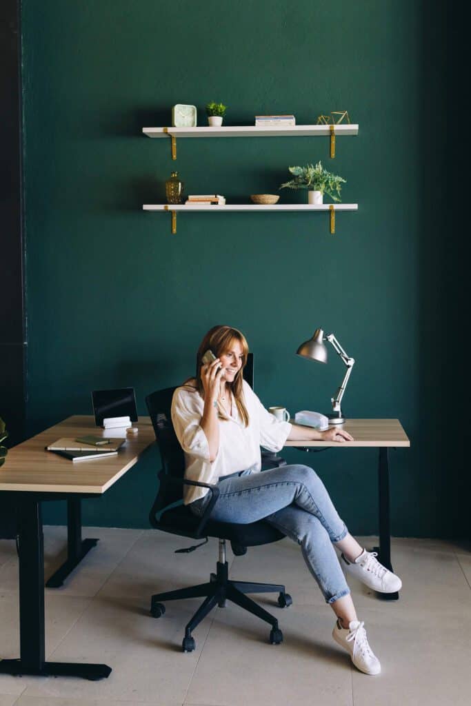 Woman sitting in a comfortable chair at an L-shaped desk, talking on the phone in an organized workspace, showing the impact of ergonomics on productivity.