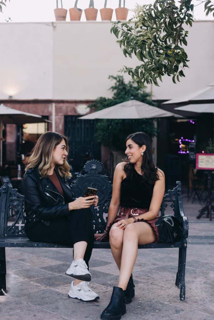 Two women sitting outside on a bench, smiling and talking, symbolizing the benefits of social support for energy and motivation.