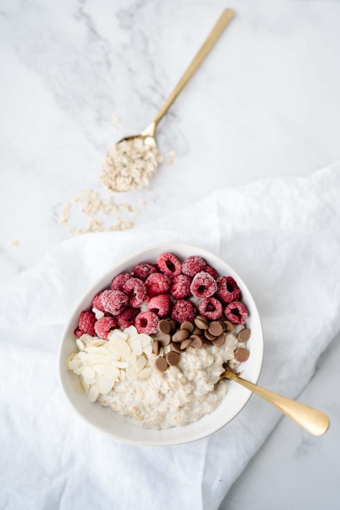 Overhead view of a bowl of oatmeal topped with raspberries, almonds, and chocolate chips, illustrating a balanced protein-packed breakfast to prevent an ADHD afternoon crash.