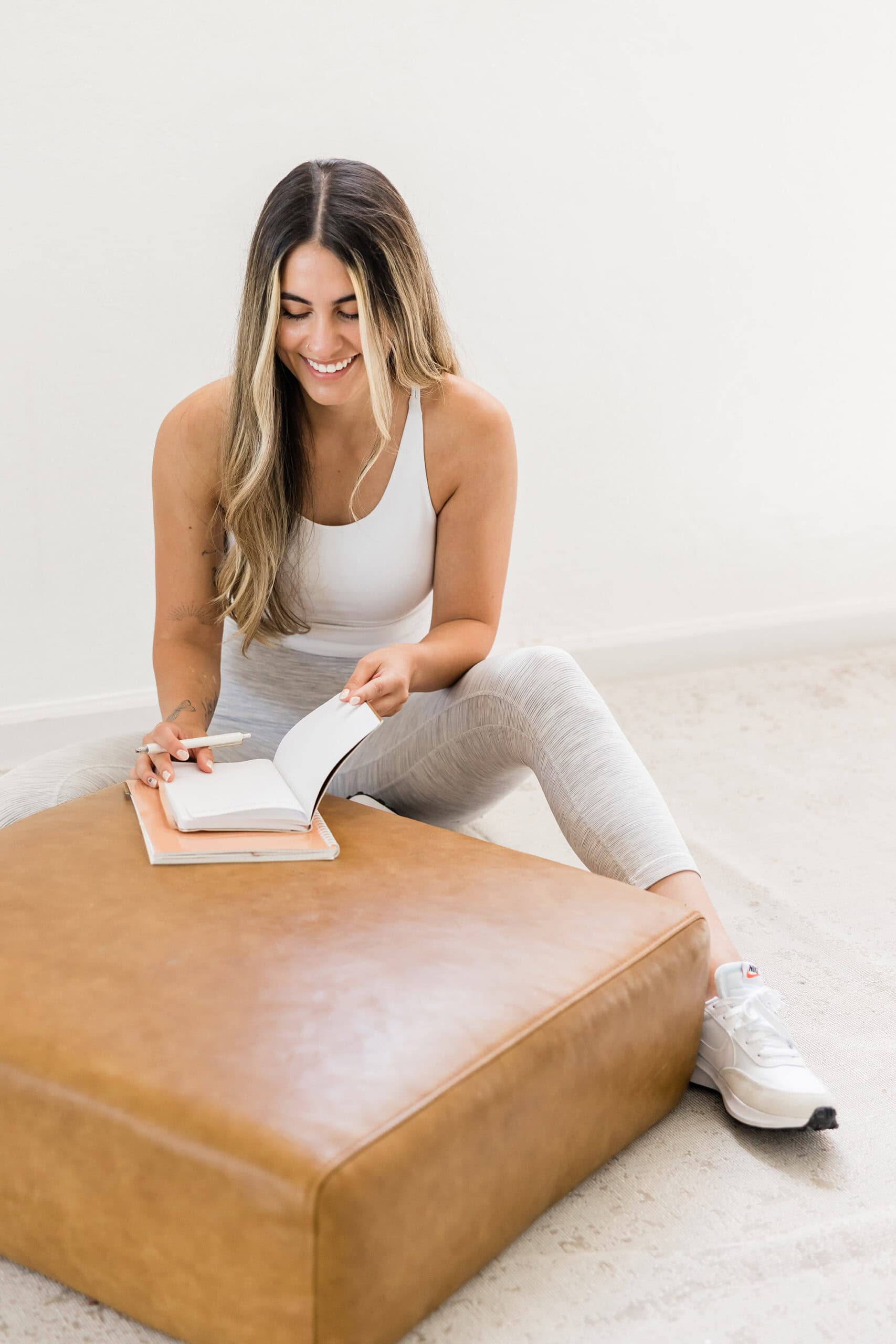 Woman sitting on the floor in workout gear, smiling while opening a journal, symbolizing calming activities for women with ADHD.