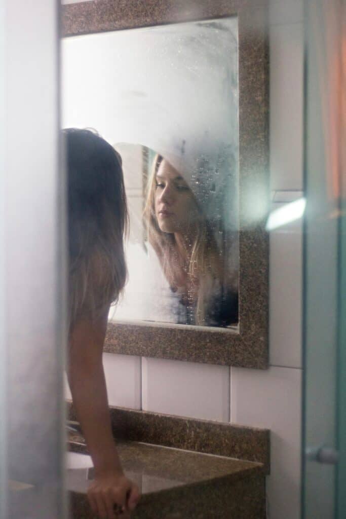 A woman reflecting on her self-image in the mirror, facing self-sabotage challenges.