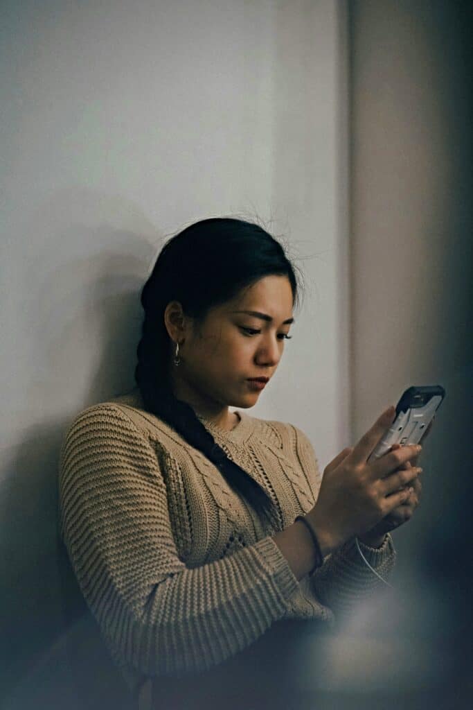 A woman scrolling on her phone, overwhelmed by social media self-sabotage.