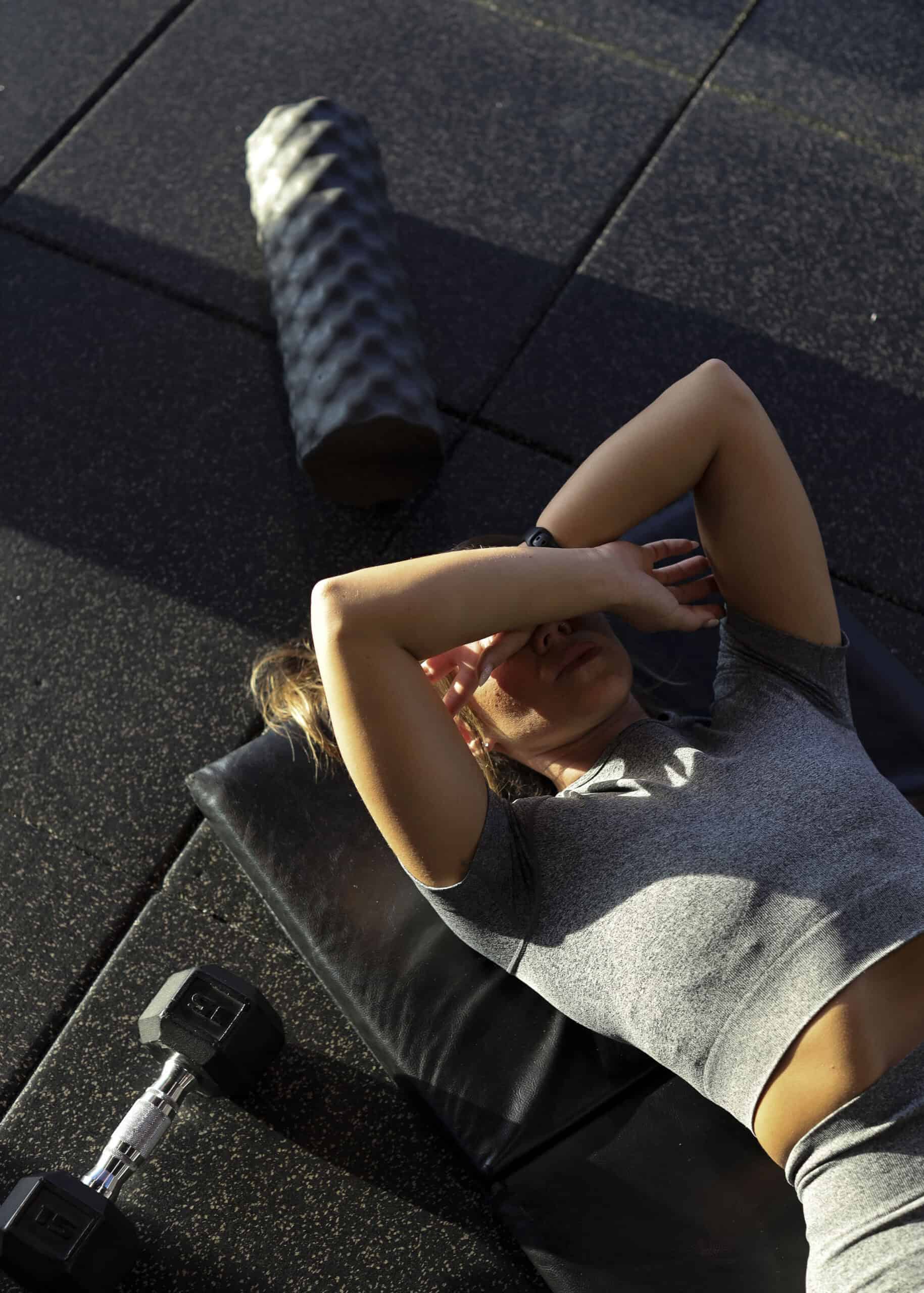 A woman lying on the gym floor with her arms crossed over her face, feeling overwhelmed after a workout.