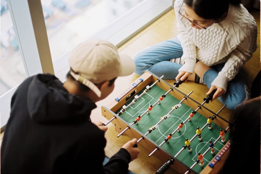 Overhead view of people playing a mini foosball table, fully engaged in the game, illustrating the value of keeping your brain active.