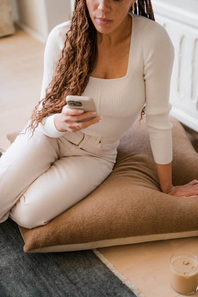 A woman sitting on the floor, scrolling through her phone, highlighting mindful digital decluttering.