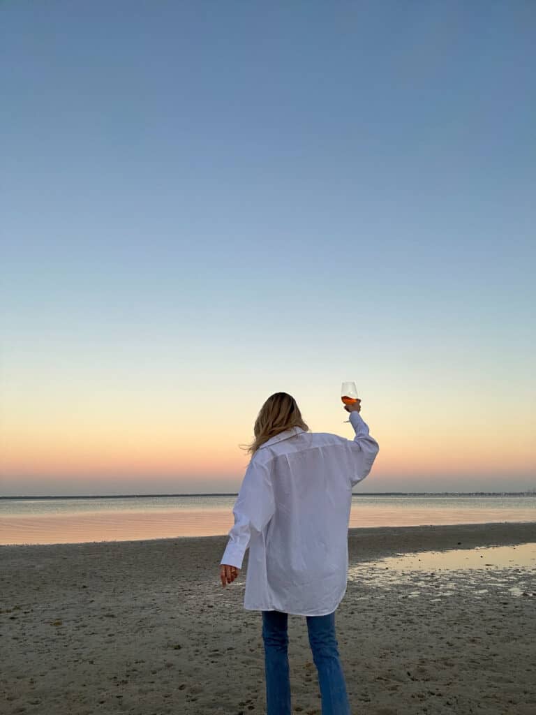 A carefree woman dancing on the beach with a wine glass, symbolizing joy and self-celebration in January.