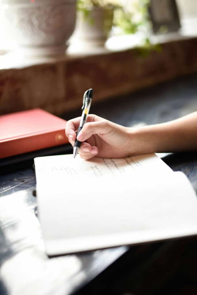 Close-up of a woman's hand writing in a notebook, illustrating the habit of daily planning for productivity.